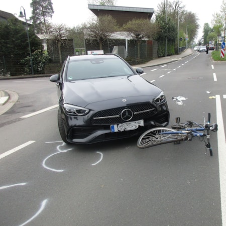 Ein Unfallauto steht neben einem schwer beschädigten Fahrrad an der Einmündung der Straße Venauen auf die Rösrather Hauptstraße.