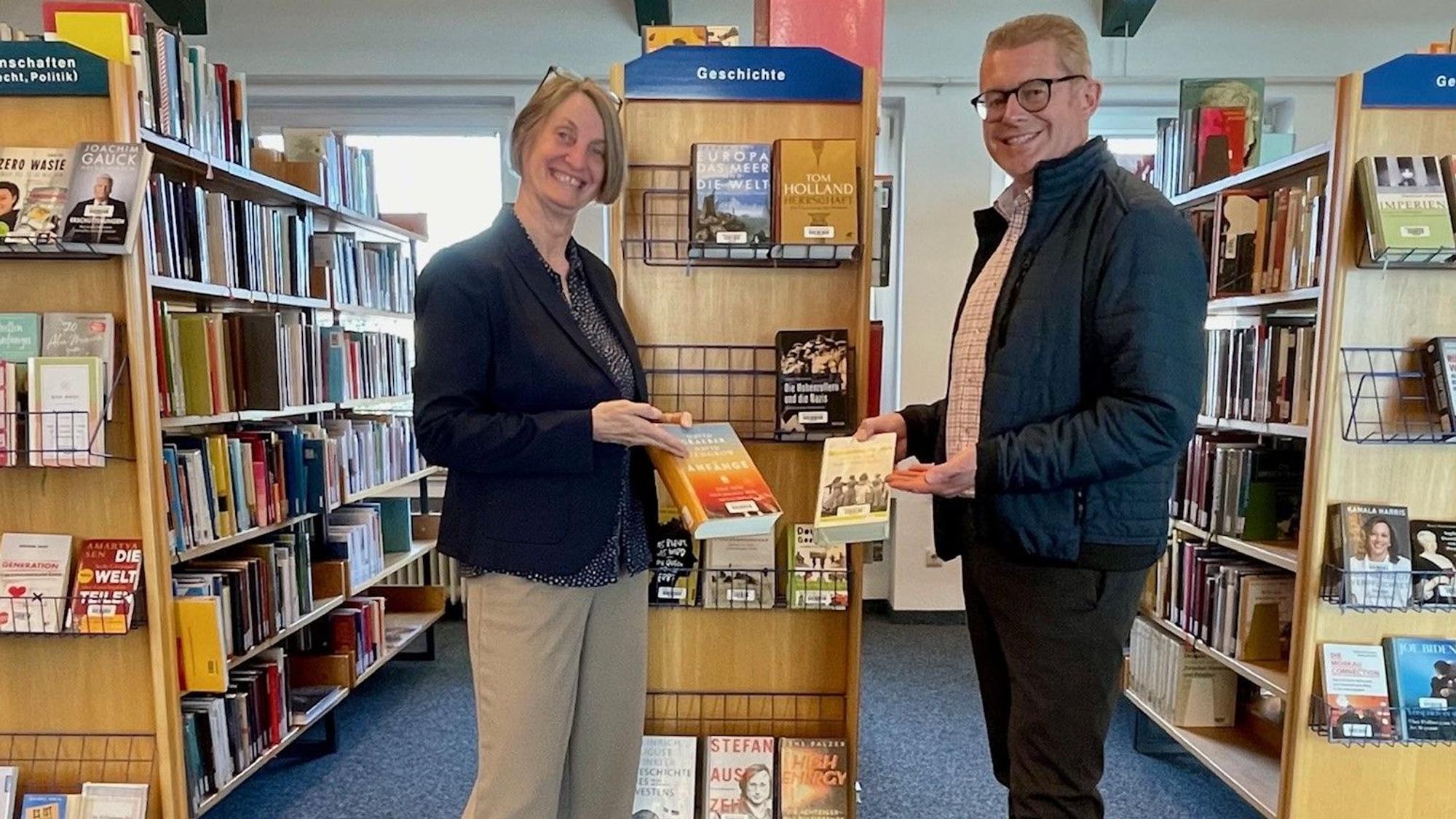 Leiterin Franzis Steinhauer steht mit dem Ersten Beigeordneten Hans-Dieter Wirtz zwischen Bücherregalen.