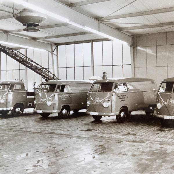 Schwarzweißbild von VW-Bullis mit Blaulicht, die 1962 in einer Halle in einer Reihe stehen.