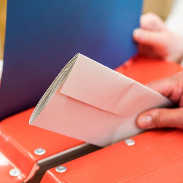 Ein Wahlhelfer steckt in einem Wahllokal den Stimmzettel eines Wählers in eine Wahlurne.