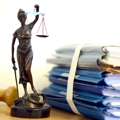 Die modellhafte Nachbildung der Justitia steht in einem Raum eines Richters neben einem Holzhammer und einem Aktenstapel.