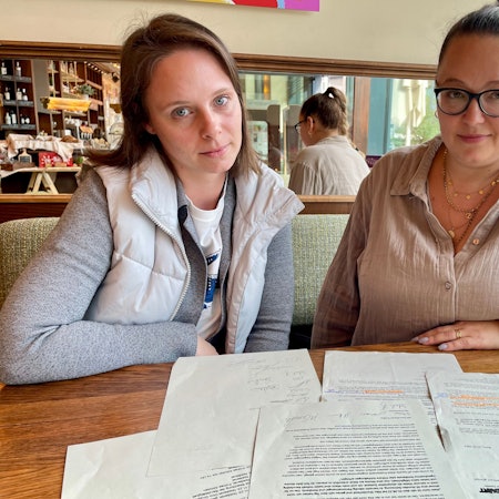 Zwei junge Frauen sitzen an einem Tisch mit Schriftstücken.