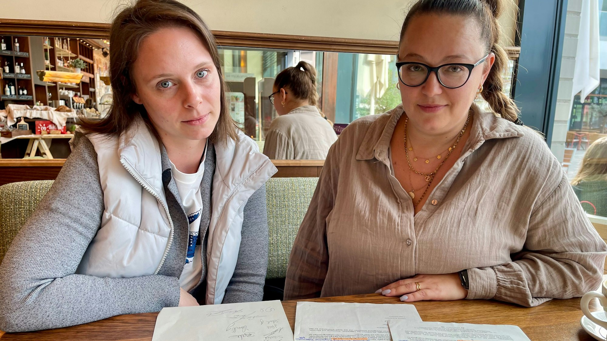 Zwei junge Frauen sitzen an einem Tisch mit Schriftstücken.