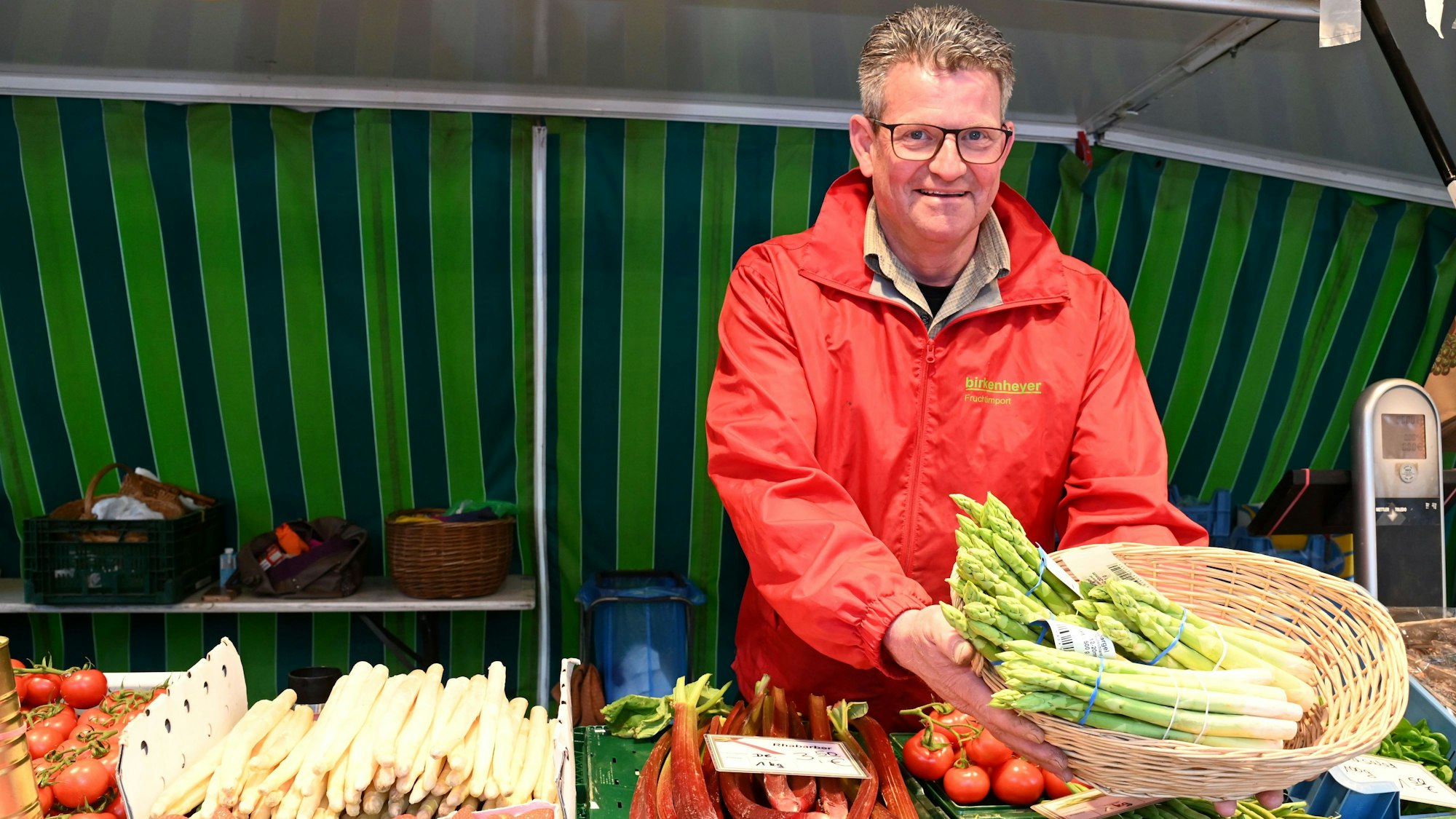 Landwirt Karl-Josef Langen steht an seinem Stand und hält einen Korb mit grünem Spargel. Foto von Alexander Schwaiger