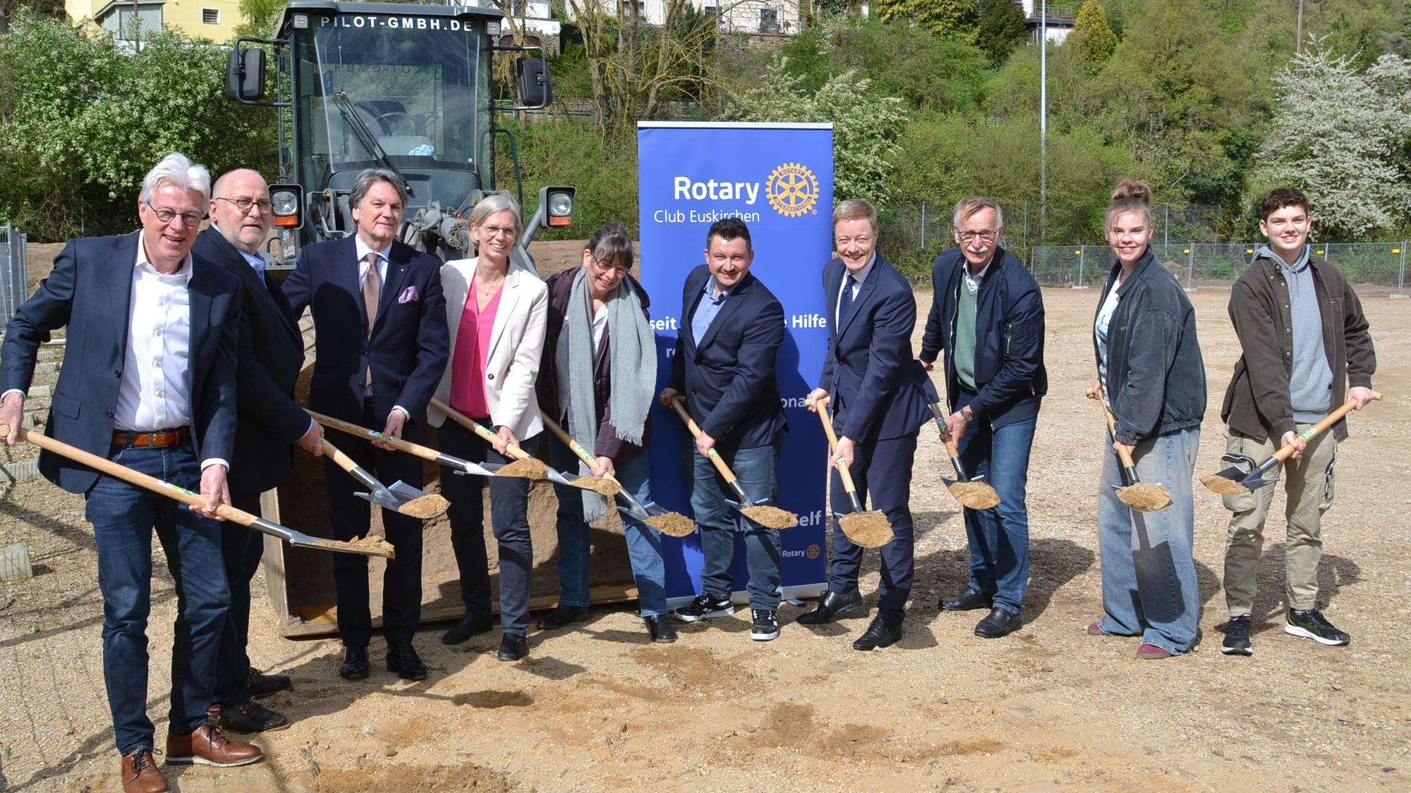 Vertreter des Rotary-Clubs und der Schule halten Schaufeln in den Händen, die mit Erde gefüllt sind.