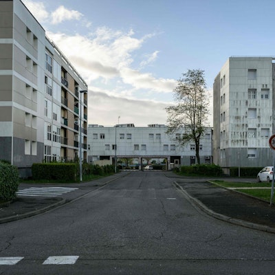 Plattenbauten und eine leere Straße befinden sich vor einem leicht bewölkten Himmel.