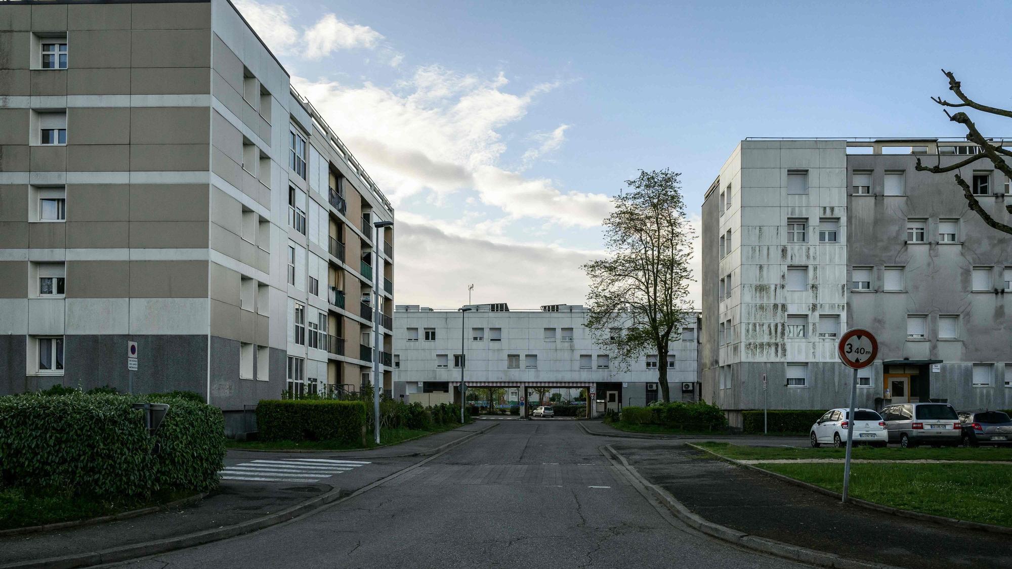 Plattenbauten und eine leere Straße befinden sich vor einem leicht bewölkten Himmel.