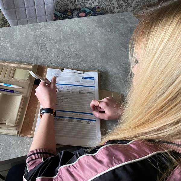 Auf einem Tisch liegt eine beigefarbene Mappe. Darin befinden sich Formulare des Weißen Rings. Yasmin Fuhl füllt die Formulare mit einem Kugelschreiber aus.