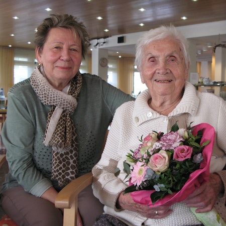 Die 102 Jahre alte Charlotte Seeger sitzt mit einem Blumenstrauß in den Händen neben ihrer 74-jährigen Tochter.