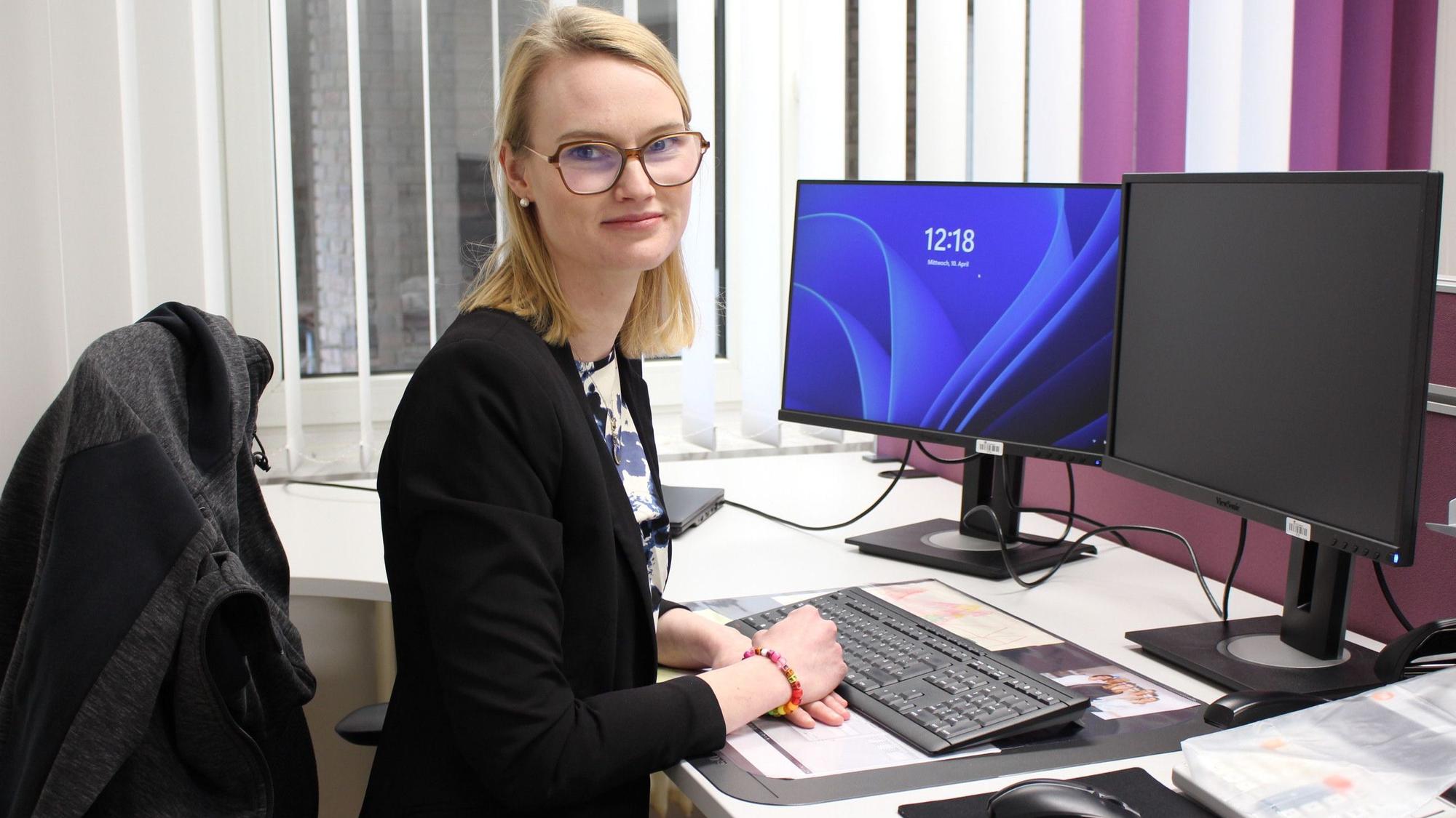 Elfi Frauenkron sitzt an ihrem Schreibtisch, vor ihr stehen Tastatur und Bildschirme.