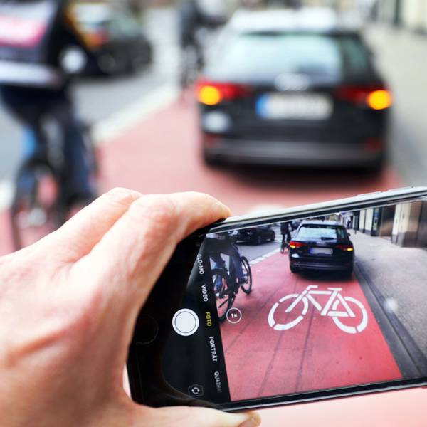 Symbolbild: Ein Auto parkt auf einem Fahrradweg, ein anderer macht ein Foto von davon.