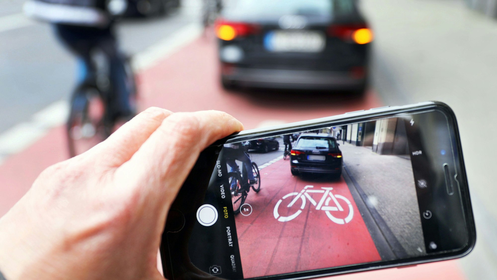 Symbolbild: Ein Auto parkt auf einem Fahrradweg, ein anderer macht ein Foto von davon.