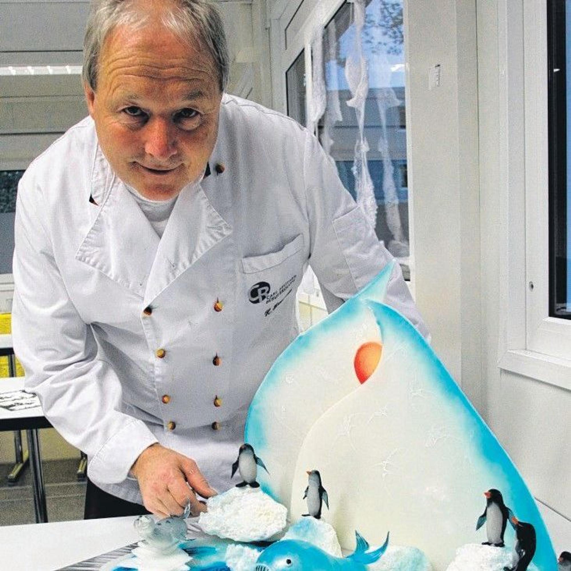 Das Bild zeigt Heiner Krautscheid in weißer Konditorjacke. Vor ihm steht eine aus Zucker geformte Südpol-Szenerie mit Eisberg, Eisschollen, Pinguinen und einem Wal.