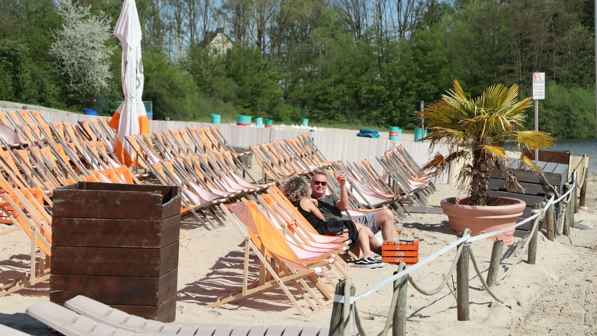 Eine Reihe von Liegestühlen am Sandstrand des Otto-Maigler-Sees. Zwei Besucher genießen schon die Sonne.