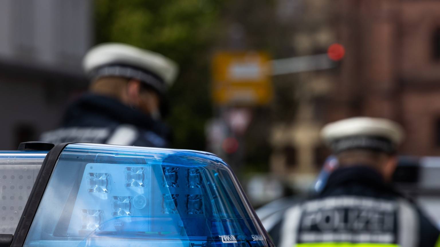 Zwei Polizeibeamte stehen zwischen zwei Einsatzfahrzeugen der Polizei.