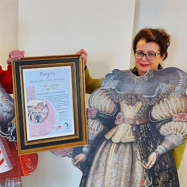 Wolfgang Doppelfeld und Dr. Ruth Kirstgen stehen hinter zwei Pappaufstellern mit historischen Kostümen.