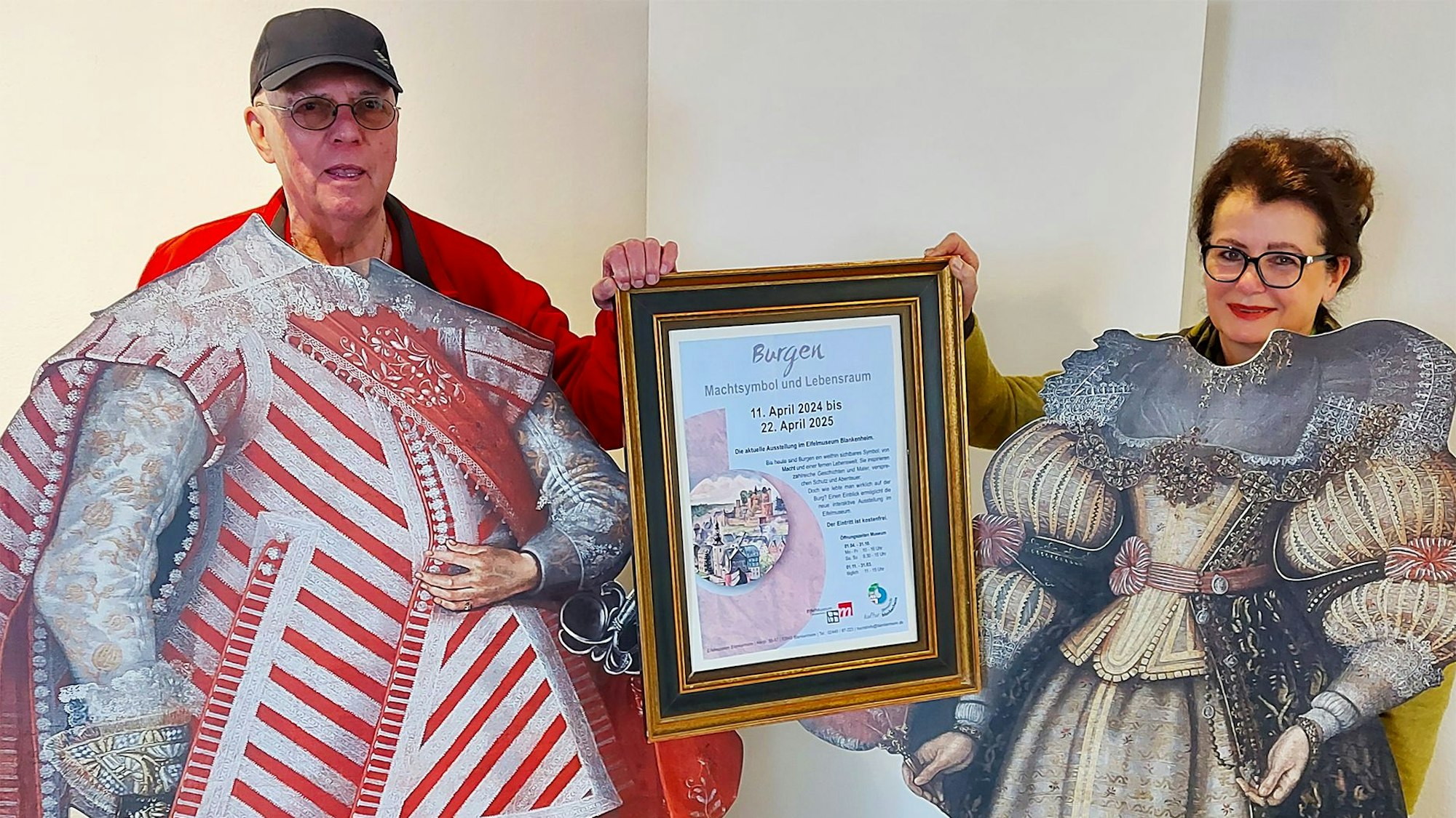 Wolfgang Doppelfeld und Dr. Ruth Kirstgen stehen hinter zwei Pappaufstellern mit historischen Kostümen.