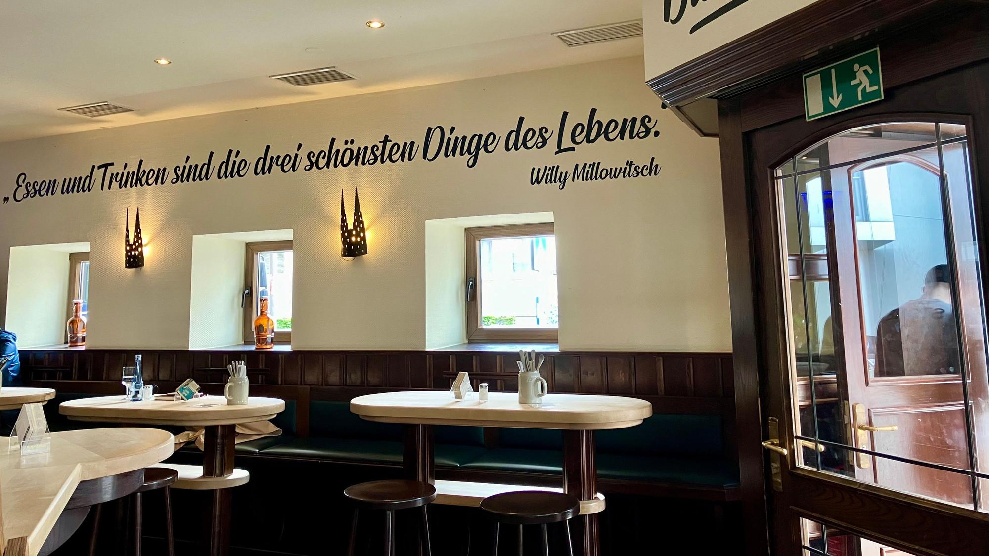Der Innenraum des Bayenthaler Wirtshaus. An der Wand ist ein Zitat von Willy Millowitsch niedergeschrieben: „Essen und Trinken sind die drei schönsten Dinge des Lebens.“ Foto von Elena Stickelmann