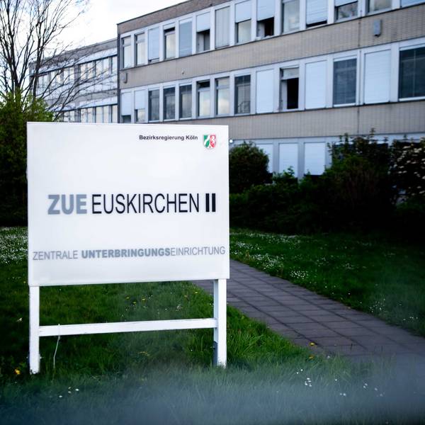 Das Bild zeigt ein Hinweisschild für die ZUE in Euskirchen. Im Hintergrund ist ein Teil des Gebäudes zu erkennen.