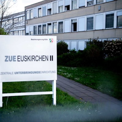 Das Bild zeigt ein Hinweisschild für die ZUE in Euskirchen. Im Hintergrund ist ein Teil des Gebäudes zu erkennen.