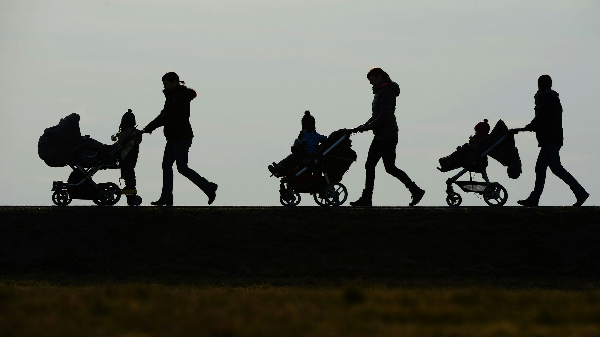 Drei Mütter schieben ihre Kinderwagen eine Straße entlang.