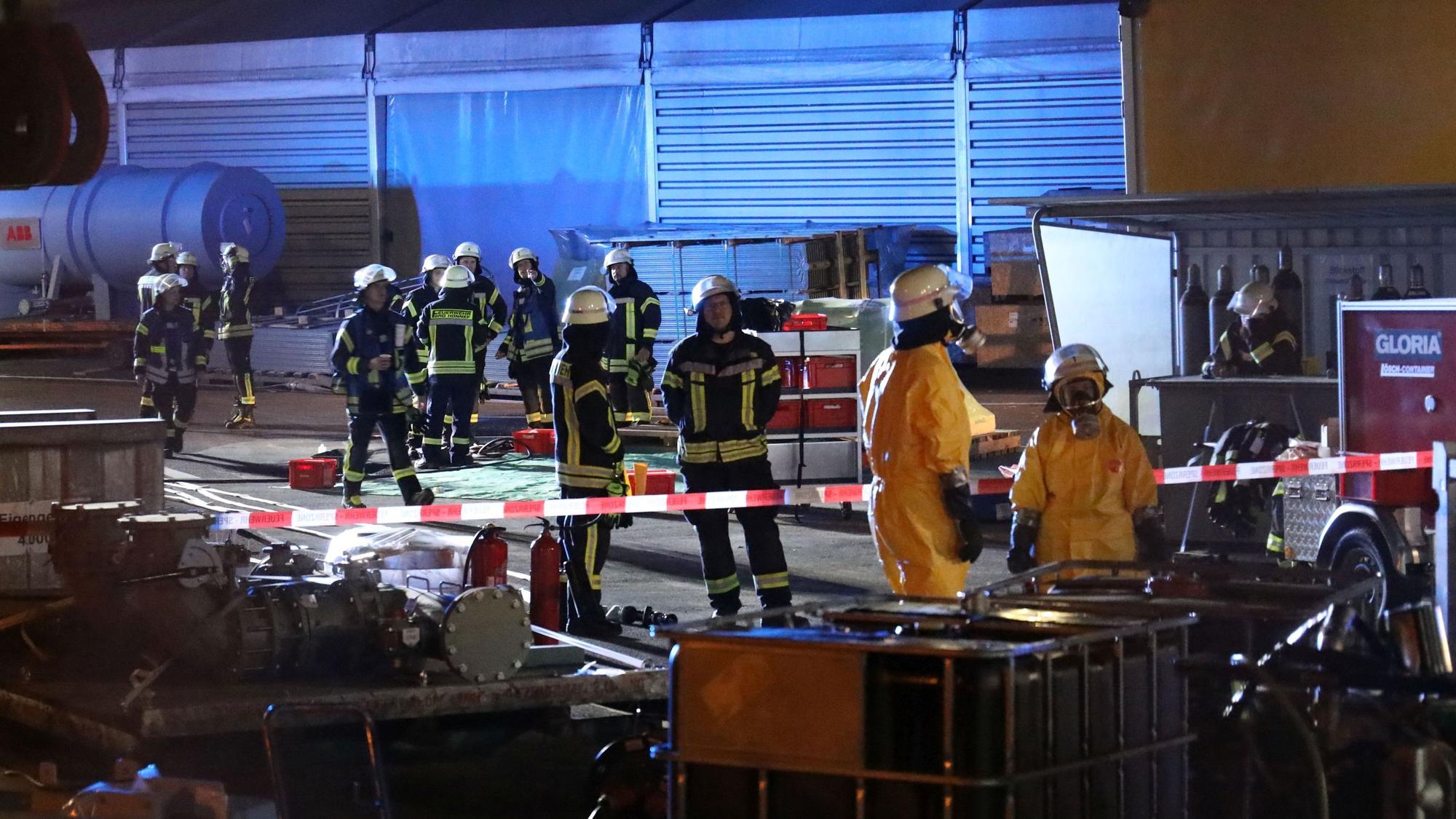 Feuerwehrleute, zum Teil in gelber Schutzkleidung, auf einem Firmengelände.