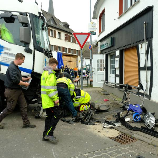 Mitarbeiter des Abschleppdienstes arbeiten am Lastwagen. Die Hauswand ist eingedrückt.