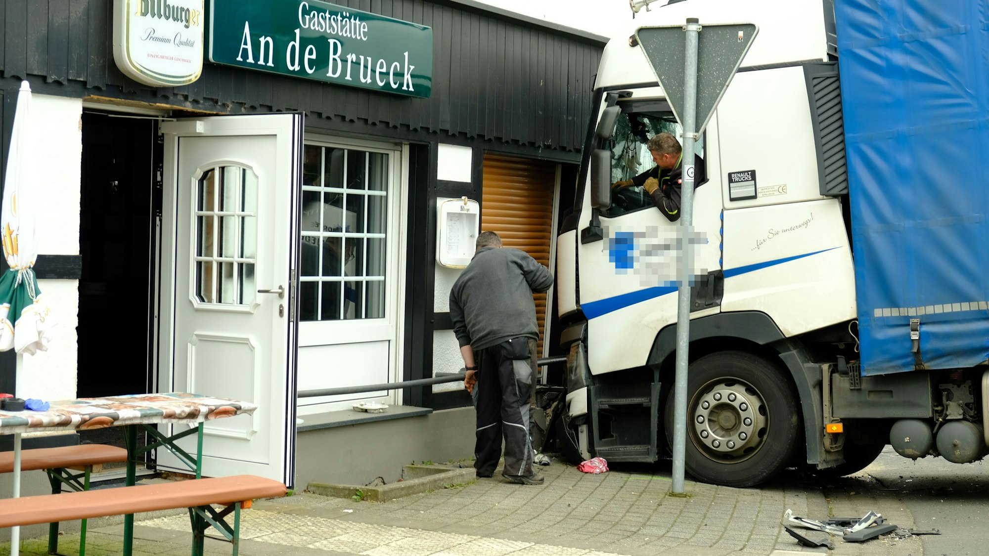 Der Lastwagen steht direkt an der Hauswand. Die Tür zur Gaststätte ist geöffnet.