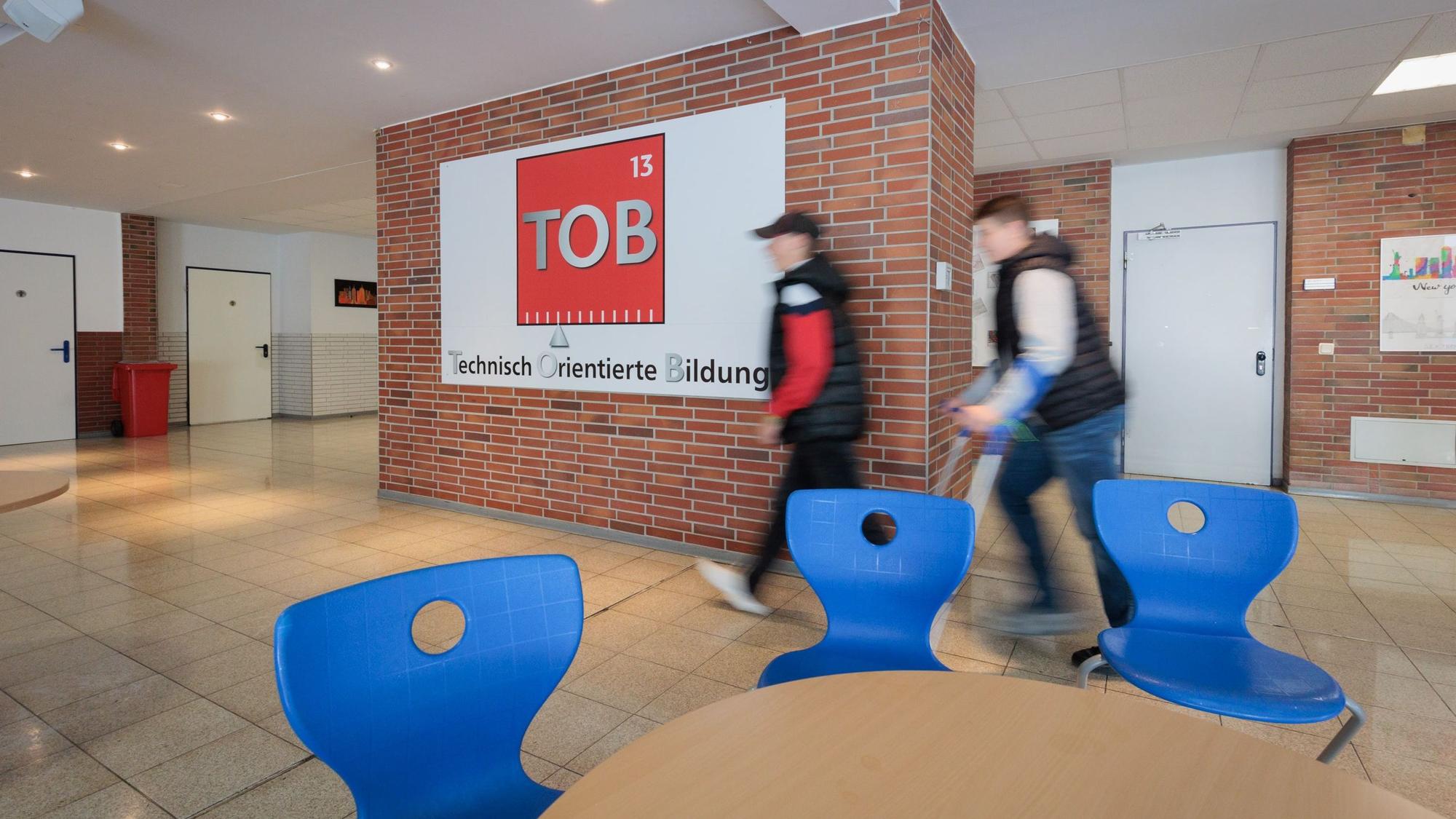 Zwei Schüler gehen am Logo der TOB Sekundarschule vorbei.