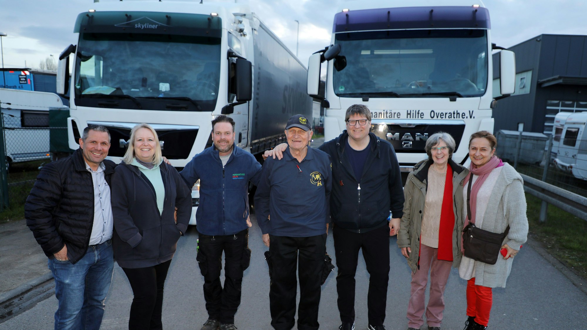 Drei Frauen und vier Männer stehen vor zwei Sattelzügen der Humanitären Hilfe Overath.