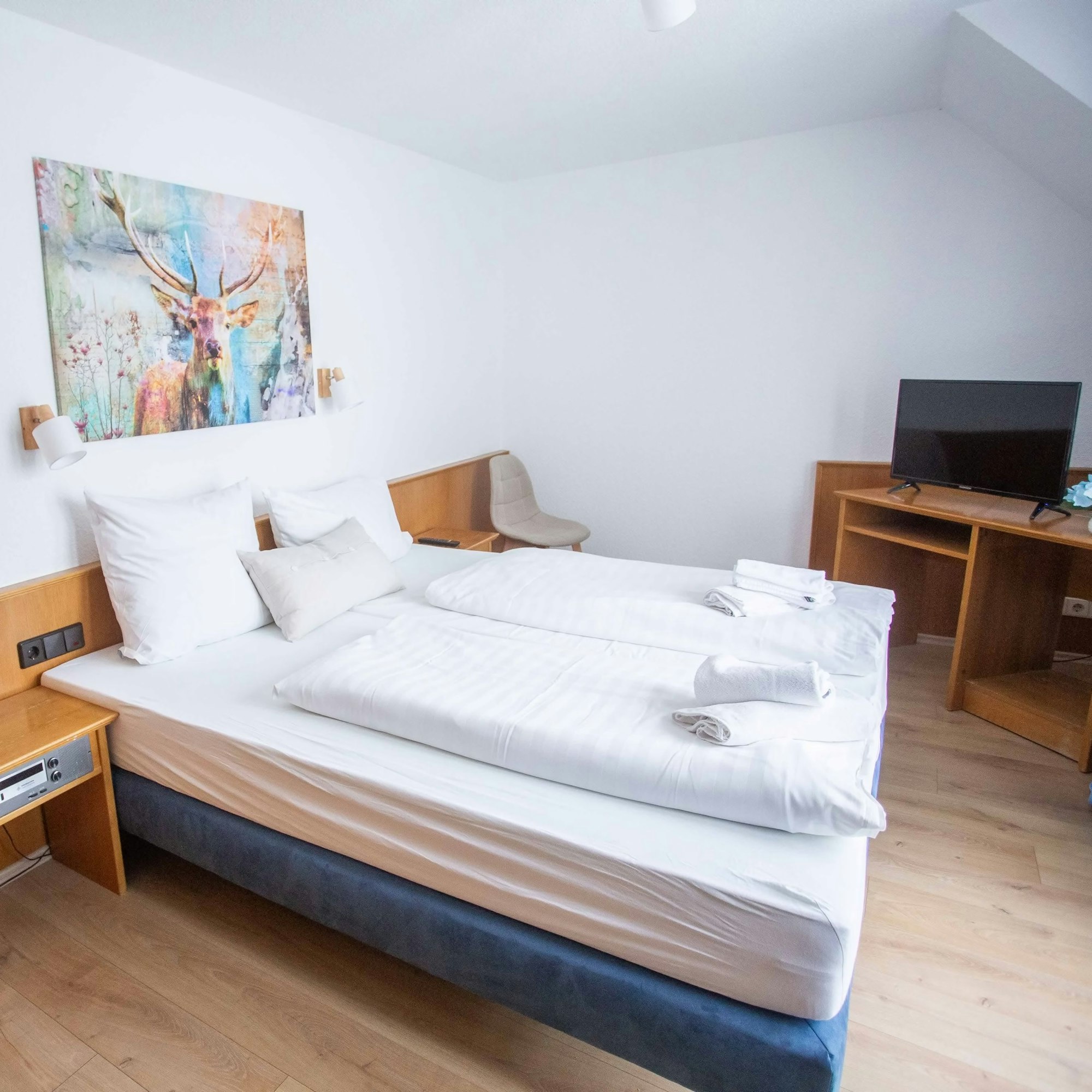 Blick in ein Hotelzimmer mit Doppelbett und einem großformatigen Kunstdruck an der Wand, der einen Hirschen zeigt.