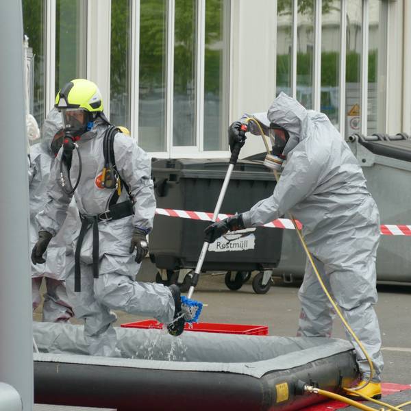 Feuerwehrleute reinigen am Dekontaminationsplatz gegenseitig ihre Schutzanzüge.