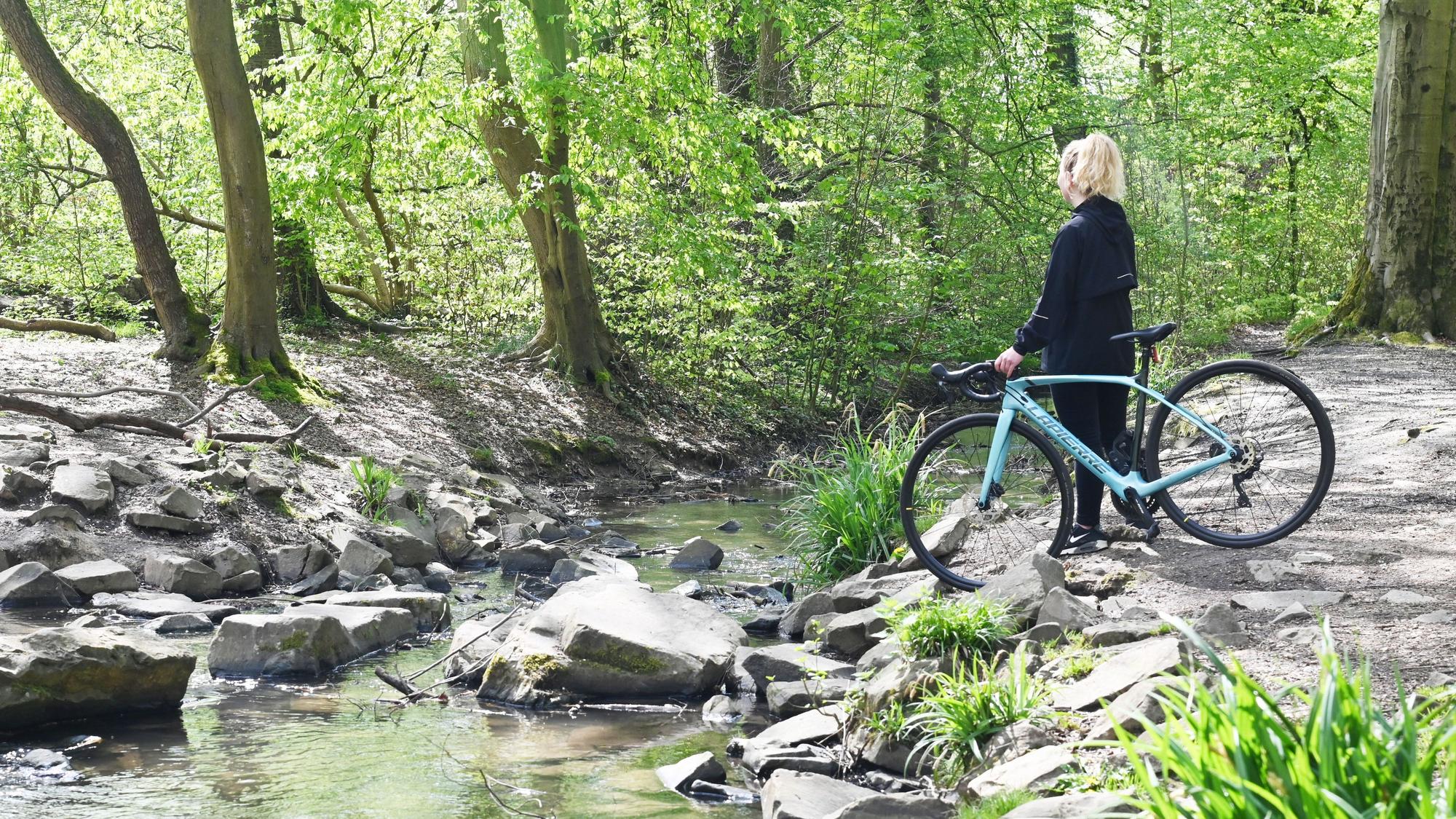 Radfahrerin steht am Wasser des Strundradwegs im rechtsrheinischen Köln