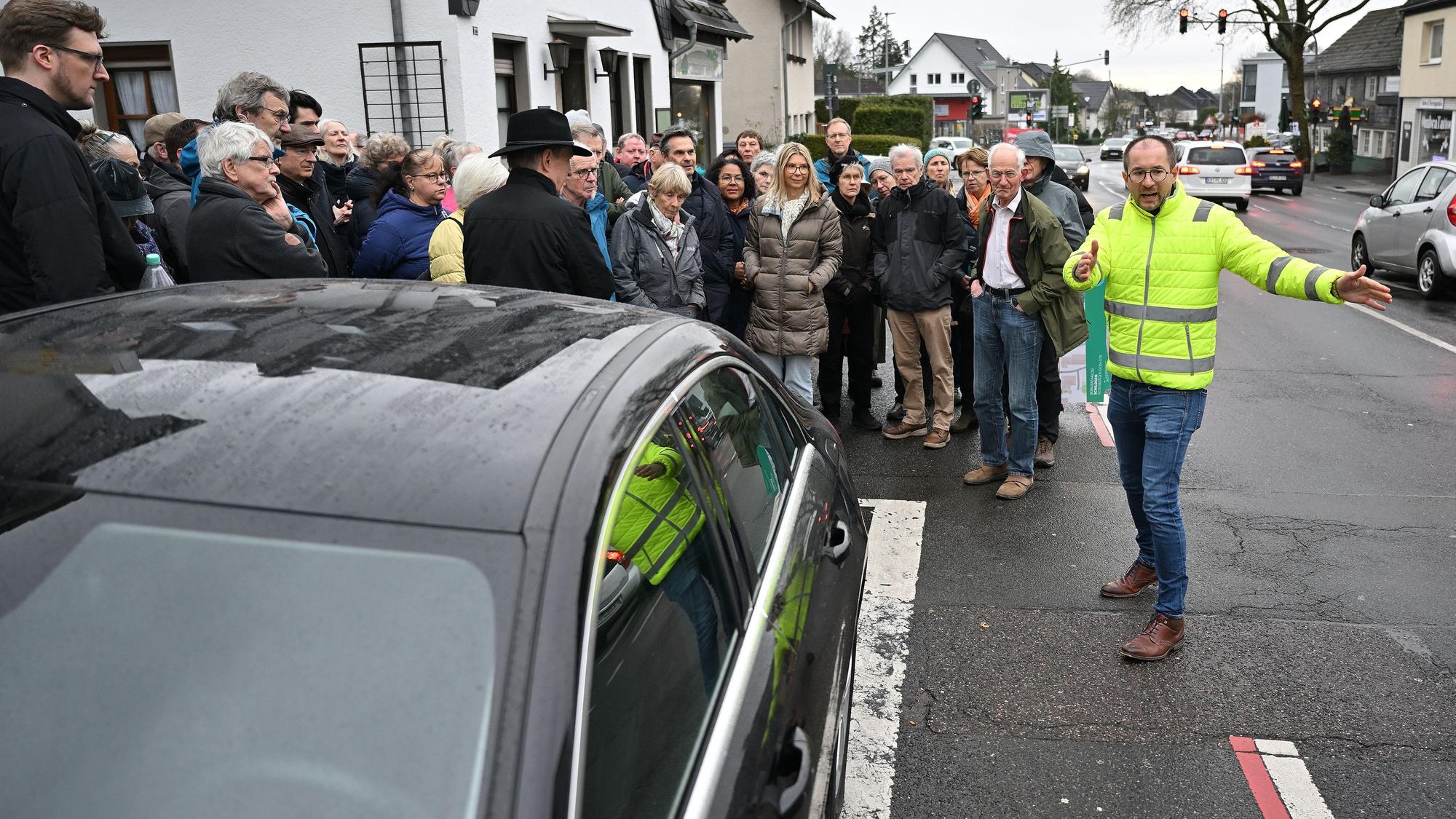 Ein Mann steht vor einer Gruppe von Bürgern am Straßenrand und erklärt etwas.
