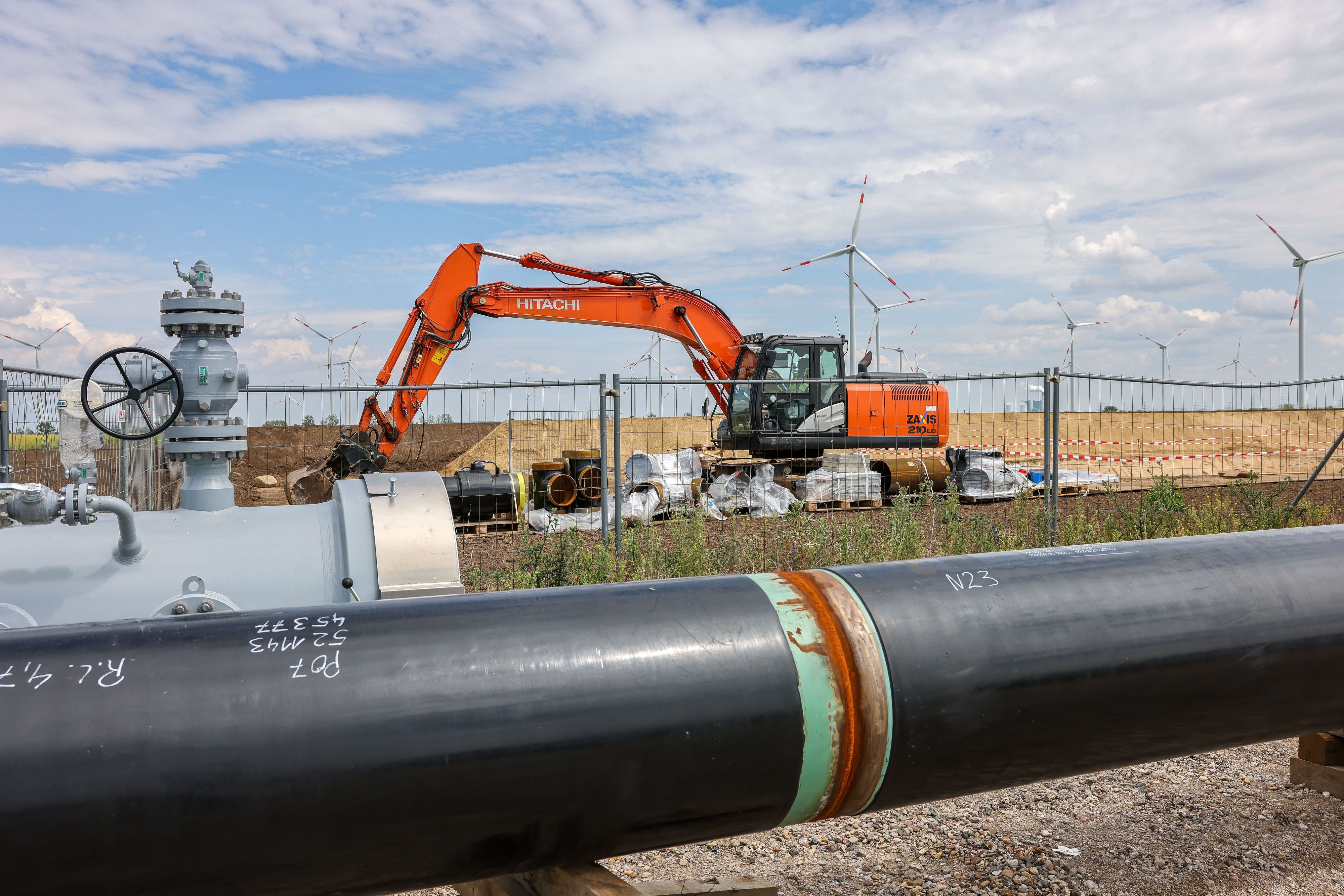 Die Rohre einer künftigen Wasserstoffleitung liegen vor der Kulisse eines Windparks.