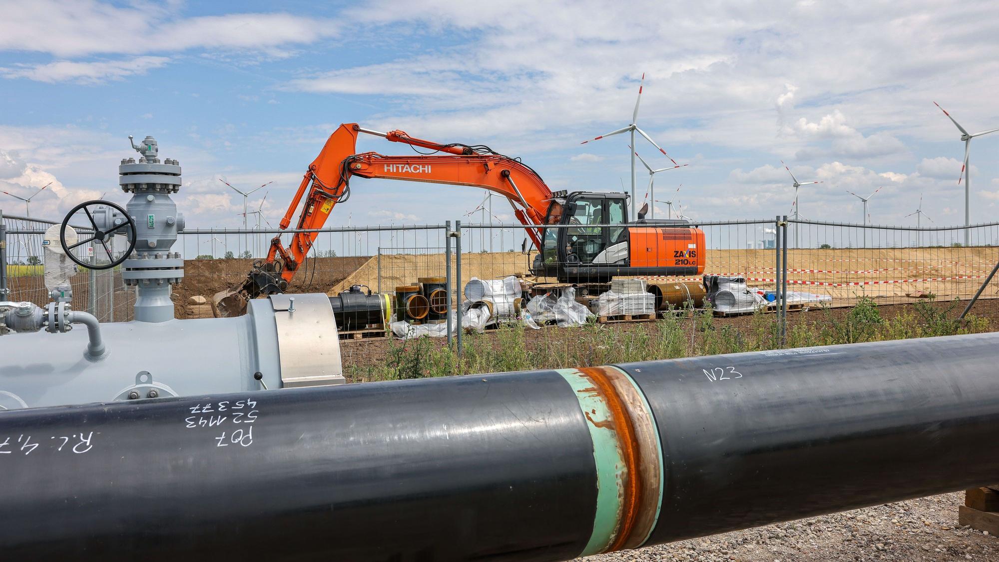 Die Rohre einer künftigen Wasserstoffleitung liegen vor der Kulisse eines Windparks.