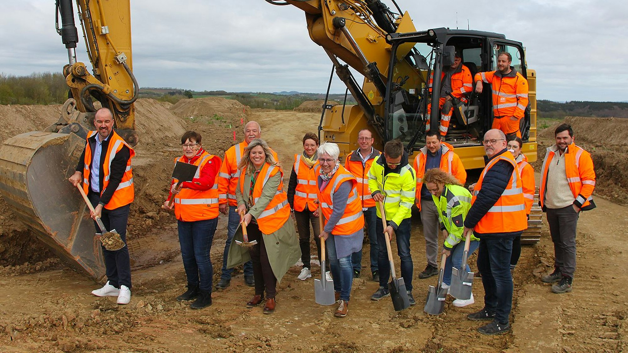 Vor einem Bagger wird der erste Spatenstich vollzogen.