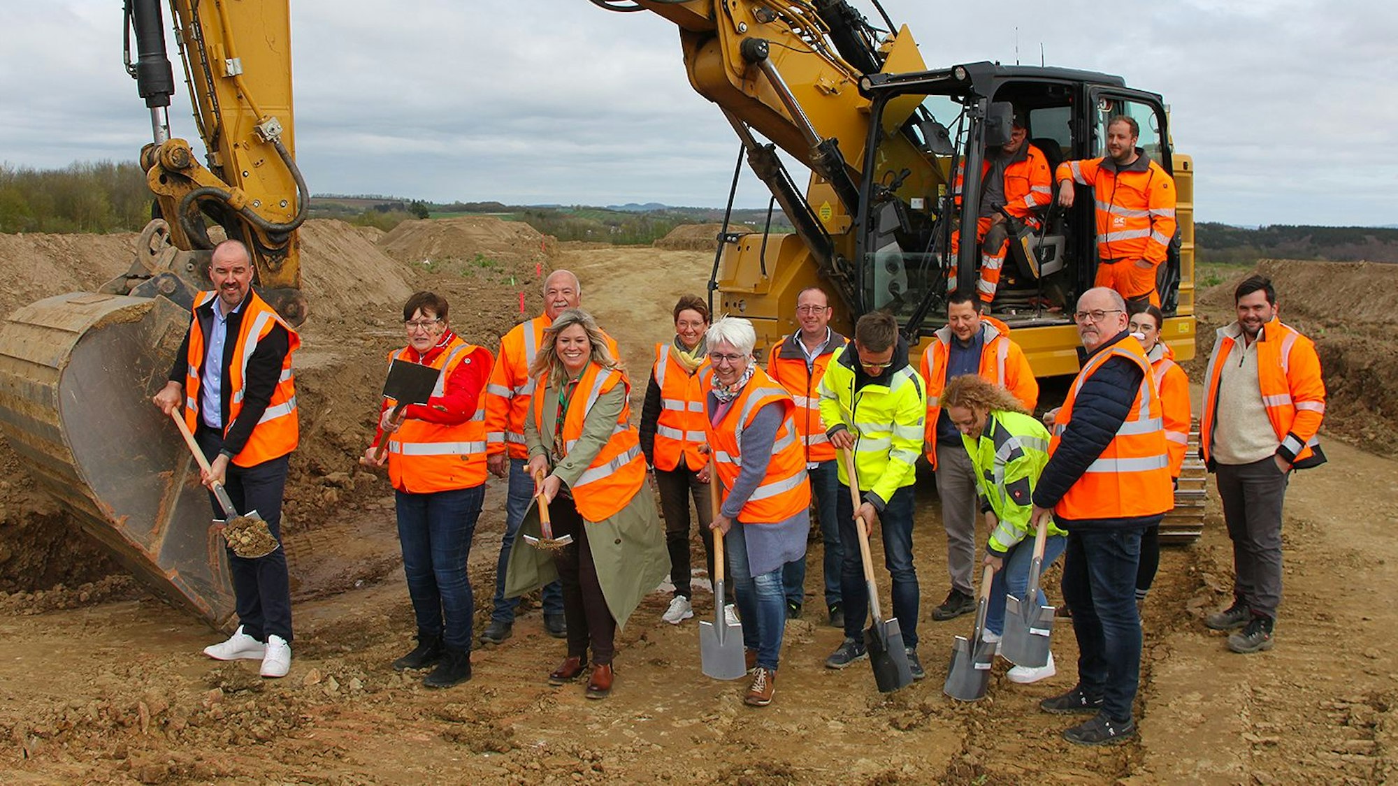 Vor einem Bagger wird der erste Spatenstich vollzogen.