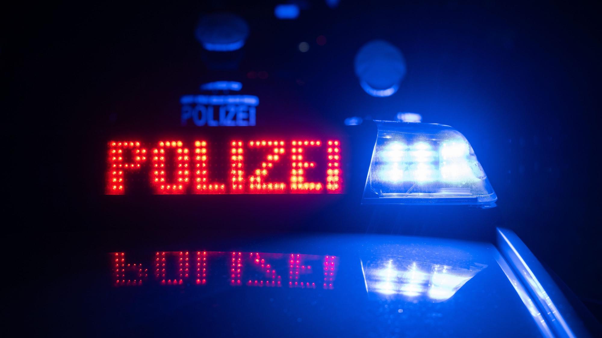 Zwei Einsatzkräfte stehen vor einem Polizeifahrzeug im Dunkeln. (Symbolbild)