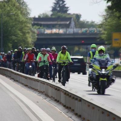 Ein dichter Pulk von Fahrradfahrern, begleitet von Polizei auf einem Motorrad.
