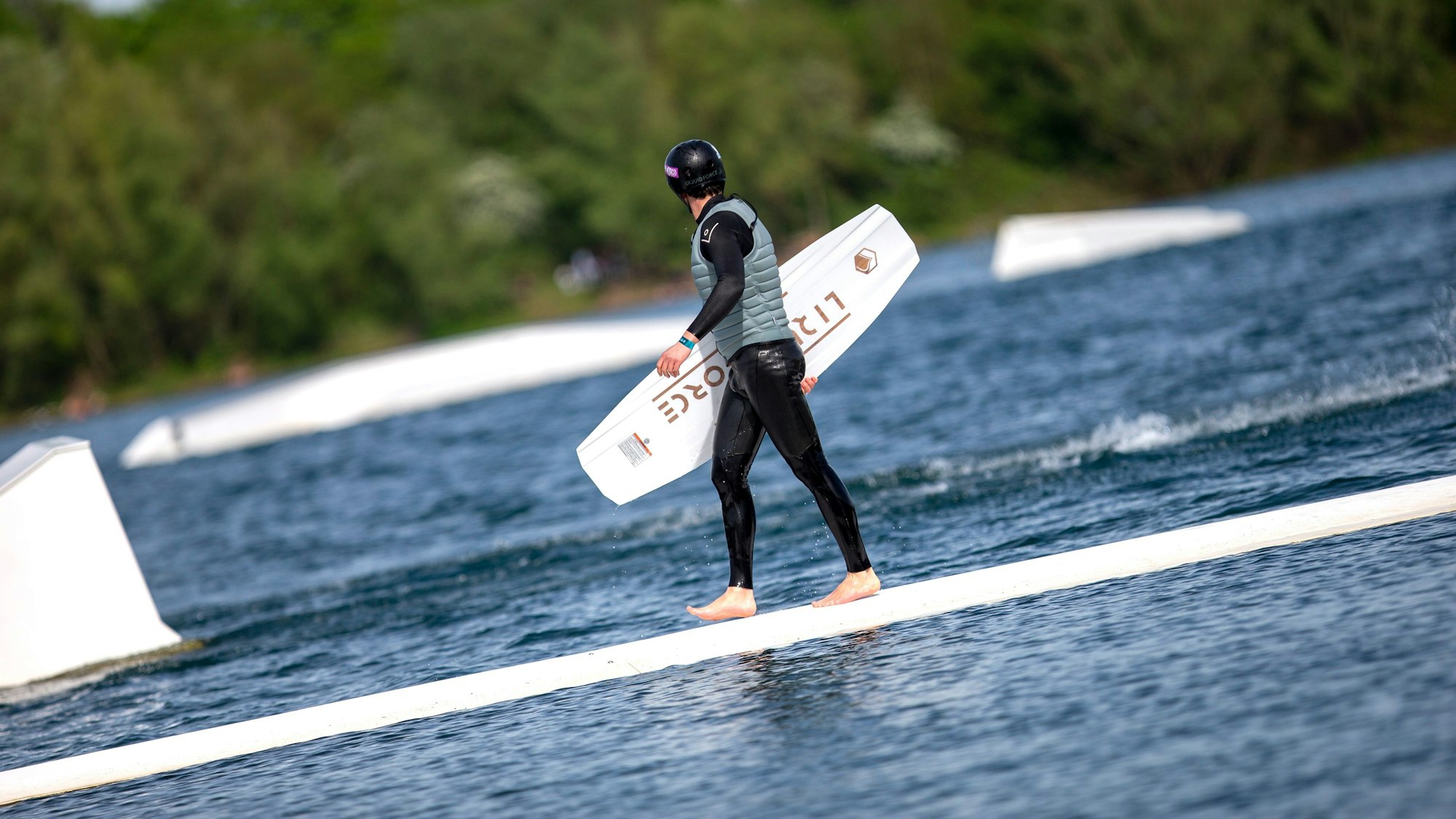 Ein Wakeboarder geht mit seinem Board in der Hand über den Rettungssteg.
