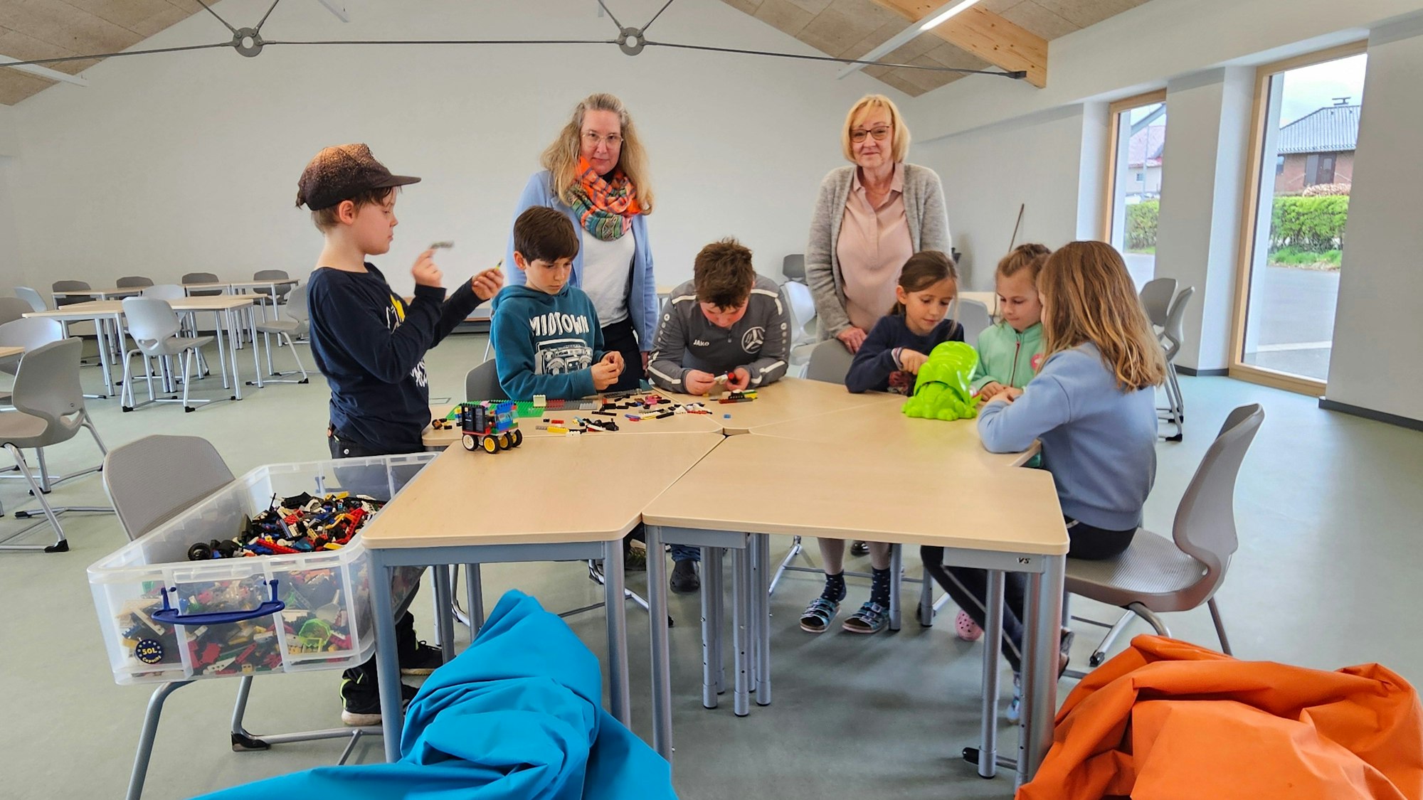 Kerstin Berners (l.) und Brigitte Wilhelms stehen hinter Kindern die an Tischen spielen.