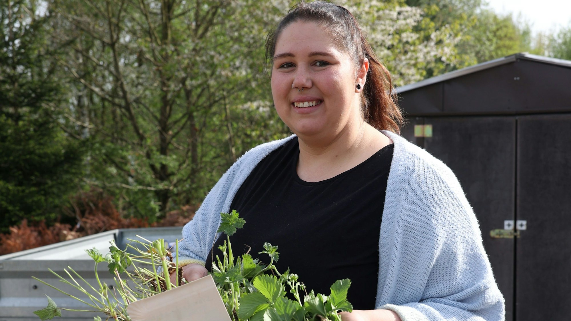Eine Frau hält einen Eimer mit jungen Pflanzen.