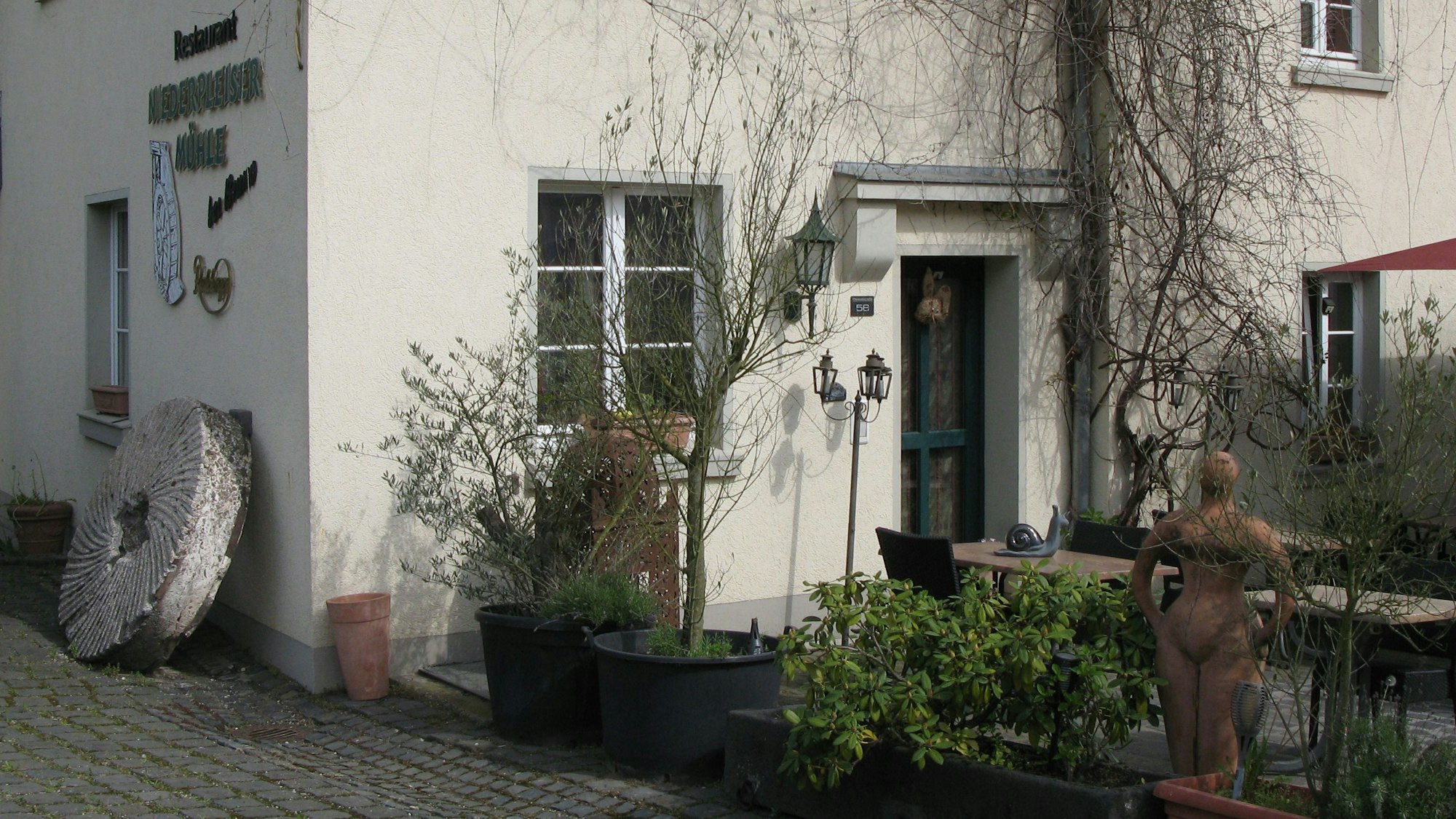 An einer Hauswand lehnt ein altes steinernes Mühlrad.