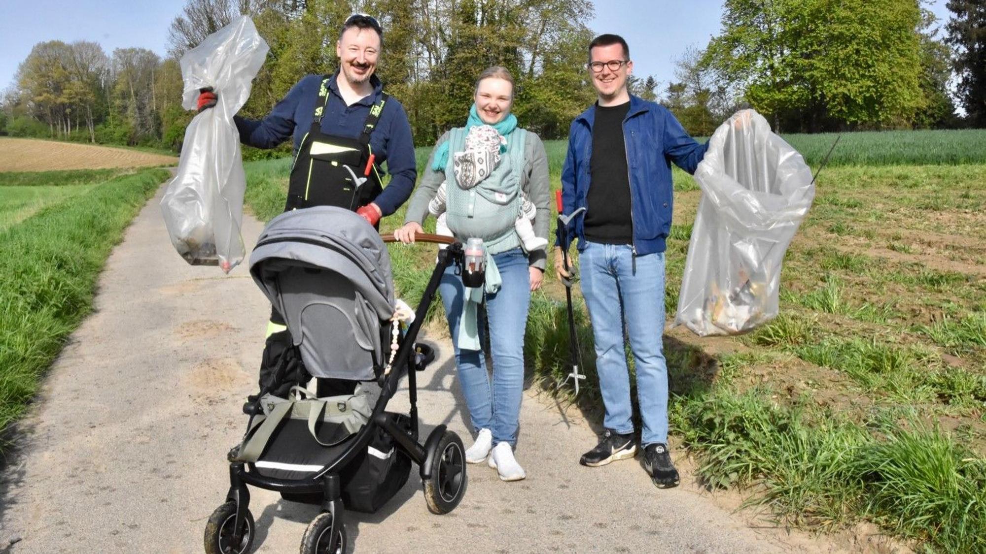 Zwei Männer halten Müllbeutel in die Höhe, zwischen ihnen steht eine Frau mit Kinderwagen und einem Baby im Tragetuch.