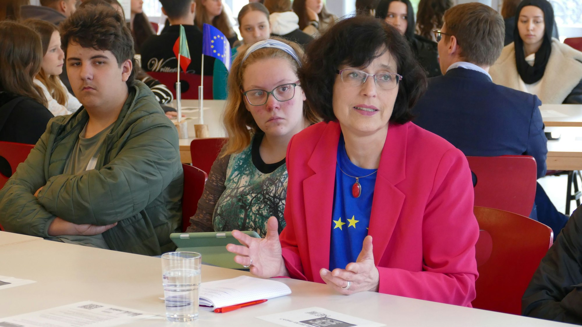 Eine Frau mit EU-T-Shirt spricht, neben ihr sitzen eine Schülerin und ein Schüler.
