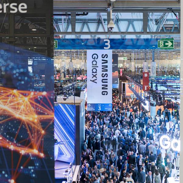 Besucher gehen durch die Messehalle auf der europäischen Mobilfunkmesse Mobile World Congress (MWC), im Vorgrund sind Schilder von Samsung Galaxy zu sehen.