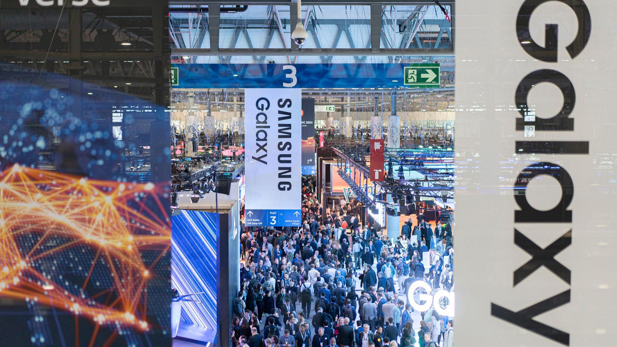 Besucher gehen durch die Messehalle auf der europäischen Mobilfunkmesse Mobile World Congress (MWC), im Vorgrund sind Schilder von Samsung Galaxy zu sehen.