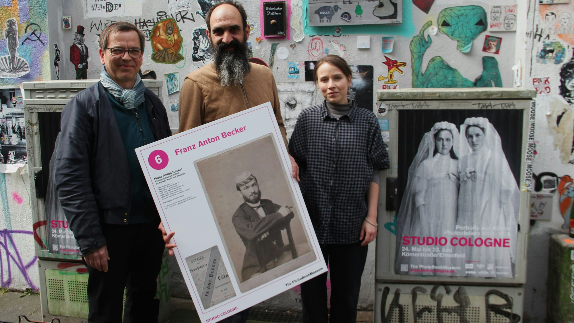 Markus Schaden, Frederic Lezmi und Leonie Serbo (v. l.) halten ein Porträt von Franz Anton Becker aus einem Kölner Photoatelier des 19. und 20. Jahrhunderts.