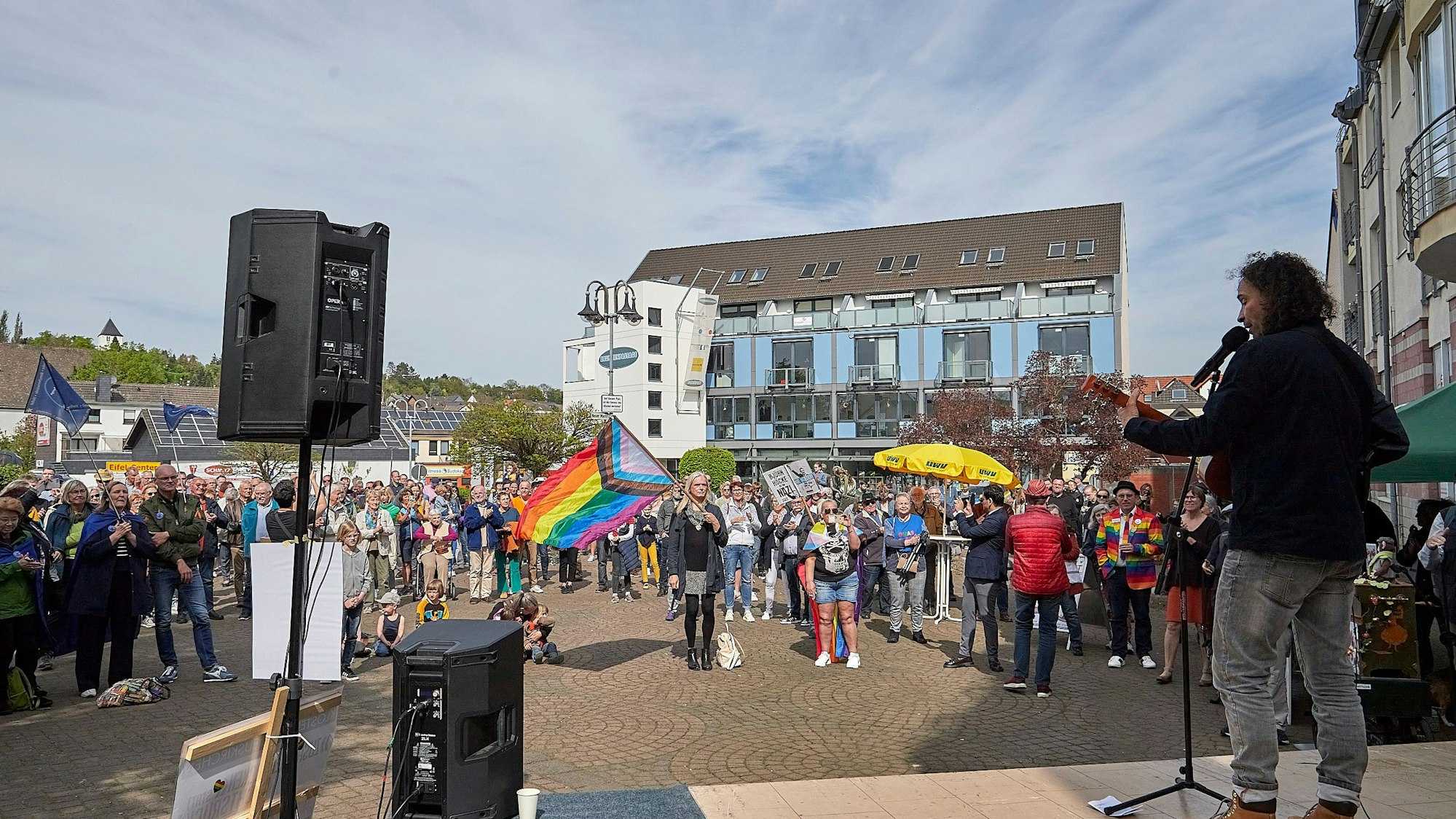 Stephan Brings steht mit der Gitarre auf der Bühne. Das Foto, das von einem Standpunkt hinter der Bühne aus gemacht wurde, zeigt zudem die Teilnehmer der Demo.